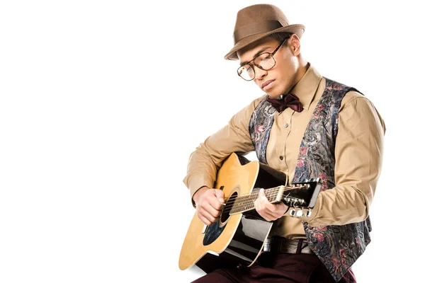 Konzentrierter gemischter Rasse männlicher Musiker mit Hut und Brille, der auf einer Akustikgitarre spielt, während er isoliert auf einem weißen Stuhl sitzt — Stockfoto