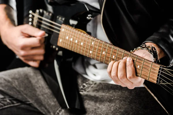 Обрезанный кадр рок-музыканта в кожаной куртке, играющего на электрогитаре, изолированной на белом — стоковое фото