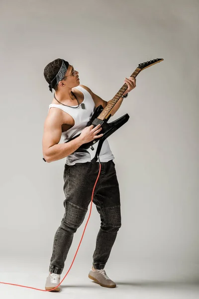 Stylish mixed race male rock musician playing on electric guitar on grey — Stock Photo