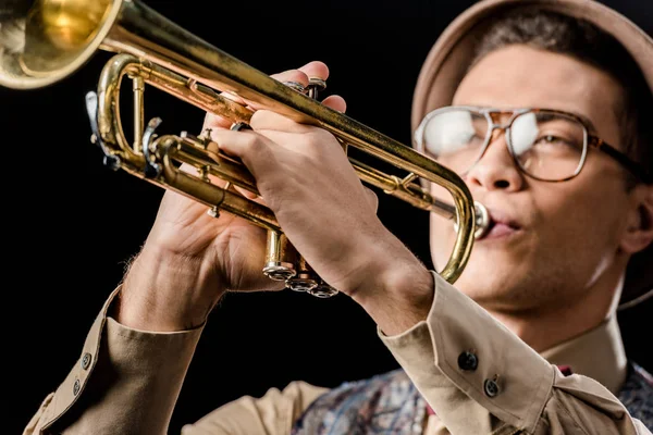 Vista da vicino di razza mista jazzman maschile in cappello e occhiali che giocano sulla tromba isolata su nero — Foto stock