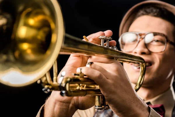 Selective focus of male jazzman in hat and eyeglasses playing on trumpet isolated on black — Stock Photo