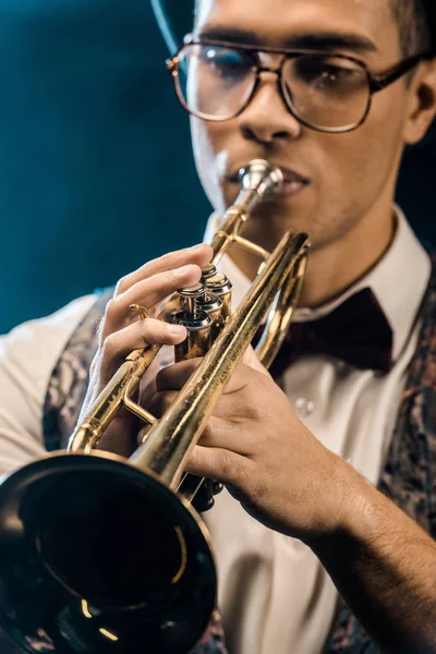 Избирательный фокус молодого джазмена, играющего на трубе на сцене с драматическим освещением и дымом — стоковое фото