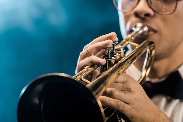 Обрізаний знімок чоловічого музиканта, який грає на трубі на сцені з драматичним освітленням і димом — стокове фото