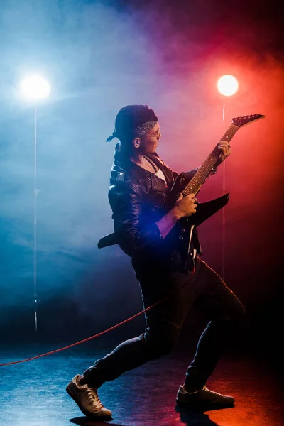 Young male musician playing on electric guitar on stage with smoke and dramatic lighting — Stock Photo