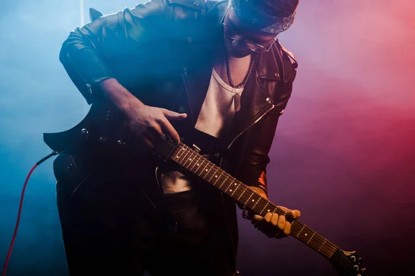 Молодий чоловік рокер в шкіряній куртці, що виступає на електричній гітарі на сцені з димом і драматичним освітленням — стокове фото