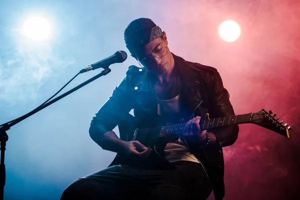 Focused male musician playing on electric guitar near microphone on stage during rock concert — Stock Photo