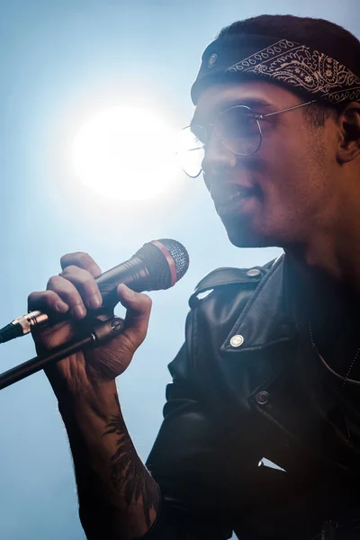 Gutaussehender männlicher Rockmusiker singt in Mikrofon auf der Bühne mit Scheinwerfer — Stockfoto