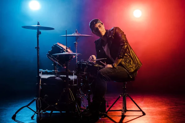 Jeune musicien mixte assis derrière le tambour mis en scène avec des projecteurs et de la fumée — Photo de stock