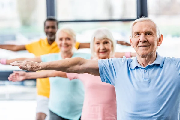 Focus selettivo di atleti anziani multiculturali sincroni che fanno esercizio in palestra — Foto stock