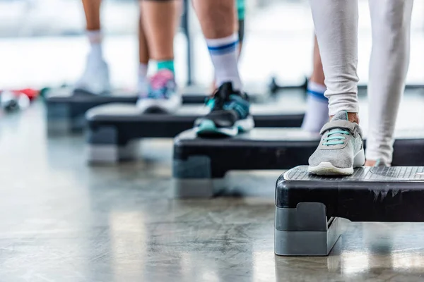 Cropped shot of sportspeople doing exercise on step platforms at gym — Stock Photo