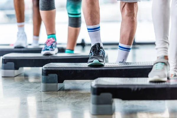 Partial view of sportspeople doing exercise on step platforms at gym — Stock Photo