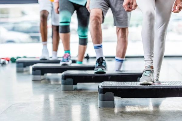 Imagen recortada de deportistas haciendo ejercicio en plataformas escalonadas en el gimnasio - foto de stock