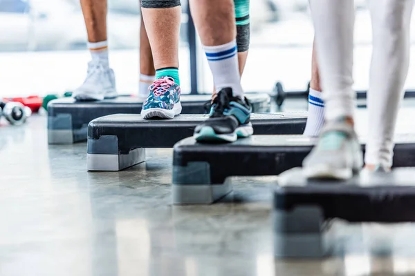 Partial view of sportspeople doing exercise on step platforms at gym — Stock Photo