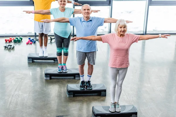 Visão de alto ângulo de atletas seniores exercício síncrono em plataformas de degrau na sala de esportes — Fotografia de Stock