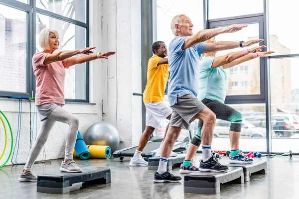Senior athletes synchronous exercising on step platforms at gym — Stock Photo