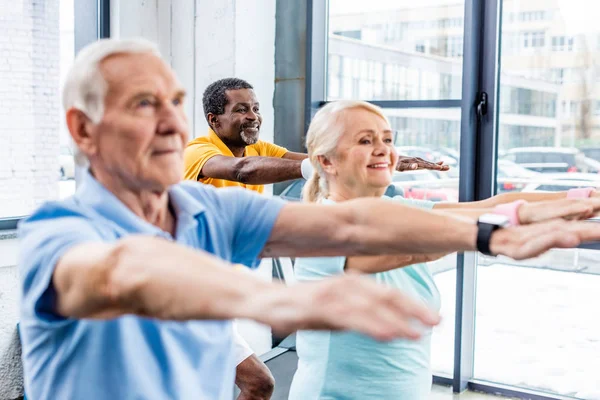 Focus selettivo di atleti anziani multiculturali sincroni che fanno esercizio in palestra — Foto stock