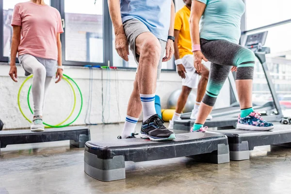 Обрезанный кадр старших спортсменов синхронных упражнений на ступенчатых площадках в тренажерном зале — стоковое фото