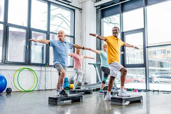 Atletas multiculturales jubilosos senior ejercicio síncrono en plataformas de paso en el gimnasio - foto de stock