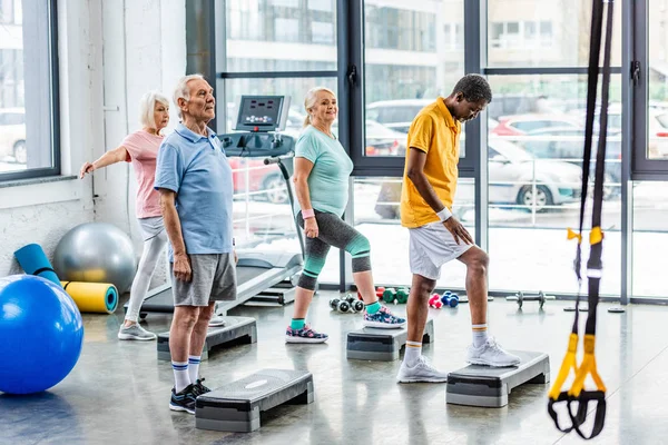 Athlètes multiethniques seniors debout près des plates-formes de marche à la salle de sport — Photo de stock