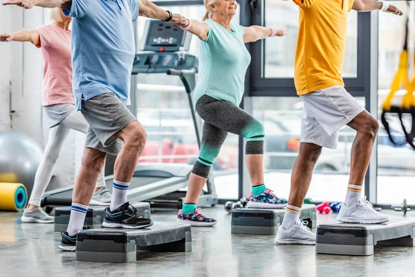 Vista parcial de los atletas senior ejercicio síncrono en plataformas de paso en el gimnasio - foto de stock