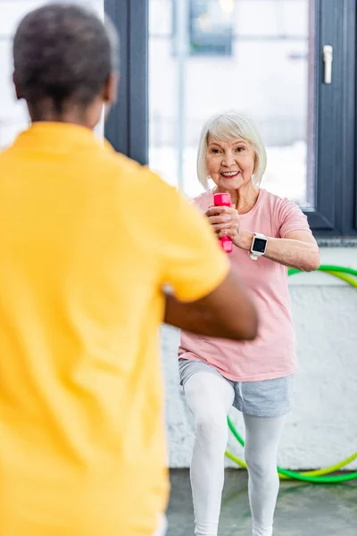 Selektiver Fokus der Seniorin mit Smartwatch bei Übungen mit der Kurzhantel im Fitnessstudio — Stockfoto