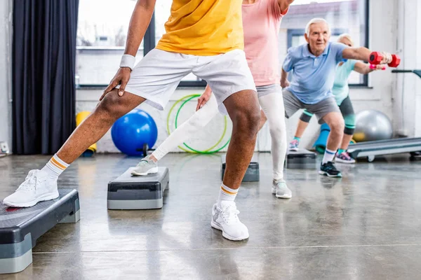 Plan recadré de sportifs seniors exercice synchrone avec haltères sur les plates-formes étape à la salle de gym — Photo de stock