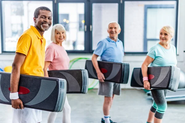 Riant sportifs multiethniques tenant plate-forme étape à la salle de gym — Photo de stock