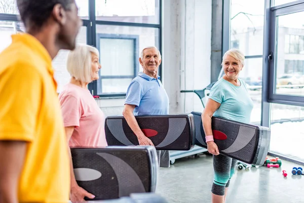 Gioiosi sportivi anziani multietnici che tengono piattaforme passo in palestra — Foto stock