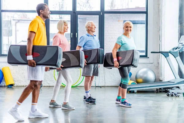 Sportifs seniors multiethniques tenant des plates-formes pas à pas à la salle de gym — Photo de stock