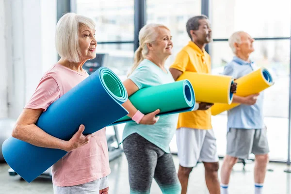 Foyer sélectif des athlètes seniors multethnic tenant des tapis de remise en forme au gymnase — Photo de stock