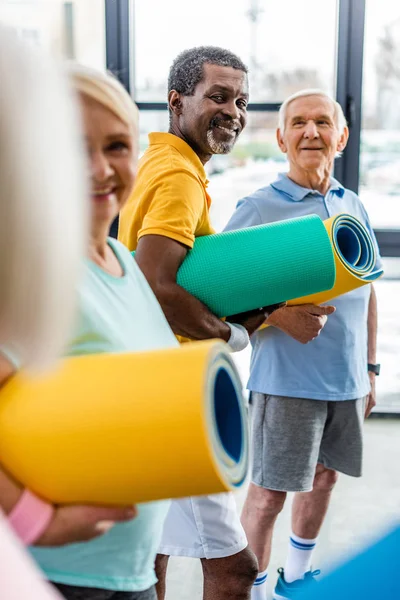 African american sportsman with fitness mat standing near friends at gym — Stock Photo