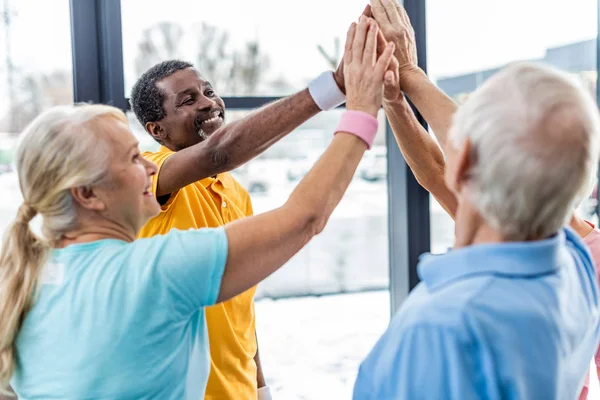 Happy senior multicultural sportspeople putting hands together at gym — Stock Photo