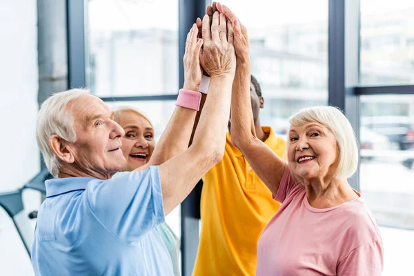 Senior happy multicultural sportspeople putting hands together at gym — Stock Photo