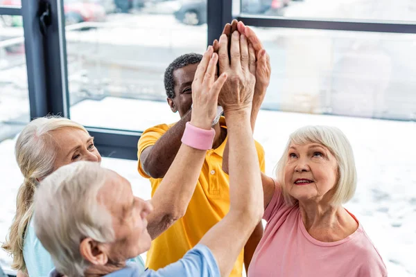 Vista de ángulo alto de deportistas multiculturales sénior poniendo manos juntas en el gimnasio - foto de stock