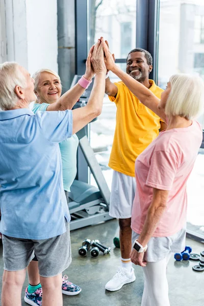 Deportistas multiculturales sénior poniendo manos juntas en el gimnasio - foto de stock