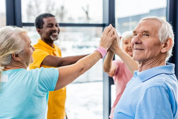 Senior man putting hands together with friends at sports hall — Stock Photo