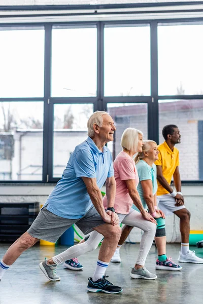 Seitenansicht der multiethnischen Senioren Synchron Stretching in der Sporthalle — Stockfoto