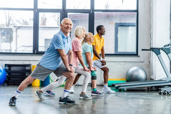 Happy senior multiethnic sportspeople synchronous stretching at sports hall — Stock Photo