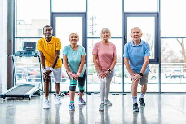 Cheerful senior multiethnic sportspeople synchronous stretching at gym — Stock Photo