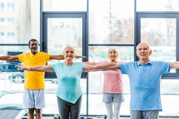 Atletas senior multiculturales sincrónicos haciendo ejercicio en el pabellón de deportes - foto de stock