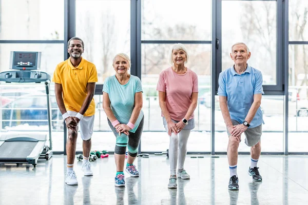 Щасливі старші багатоетнічні спортсмени синхронно розтягуються в спортивному залі — стокове фото