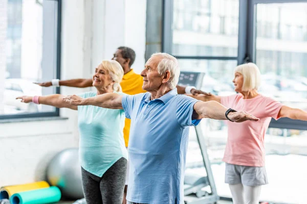 Atletas multiétnicos senior síncrona haciendo ejercicio en el pabellón de deportes - foto de stock