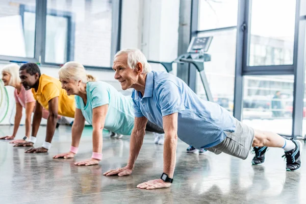 Multikulti-Senioren synchron beim Planken im Fitnessstudio — Stockfoto