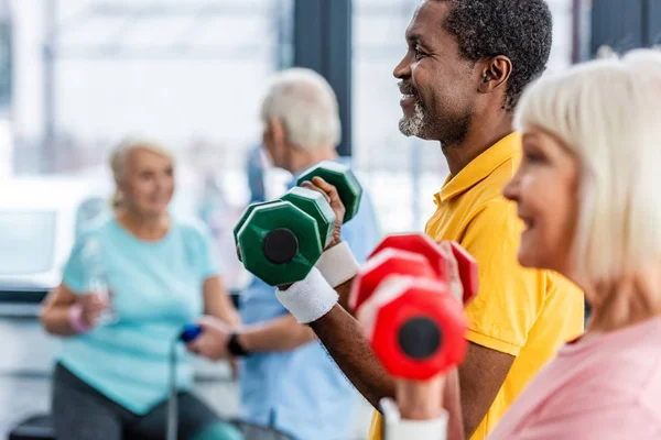 Selektiver Fokus eines reiferen interrassischen Paares bei Übungen mit Hanteln im Fitnessstudio — Stockfoto