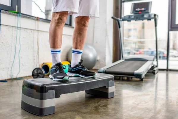 Imagem cortada de atleta masculino sênior em pé na plataforma passo no ginásio — Fotografia de Stock