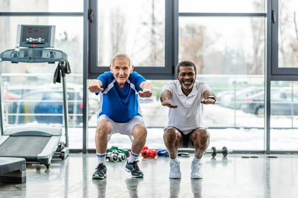 Happy multicultural mature sportsmen doing squats at gym — Stock Photo