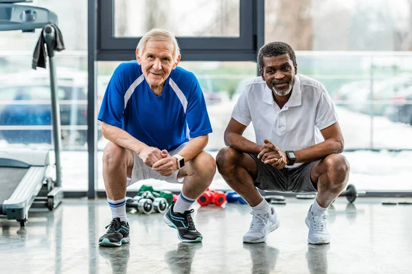 Smiling multiethnic sportsmen looking at camera and sitting at sports hall — Stock Photo