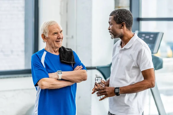 Multicultural mature sportsmen talking to each other during rest at gym — Stock Photo