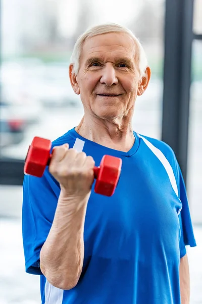 Sonriente deportista senior haciendo ejercicio con mancuerna en el gimnasio - foto de stock
