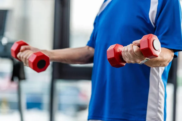 Cropped image of senior sportsman exercising with dumbbells at gym — Stock Photo
